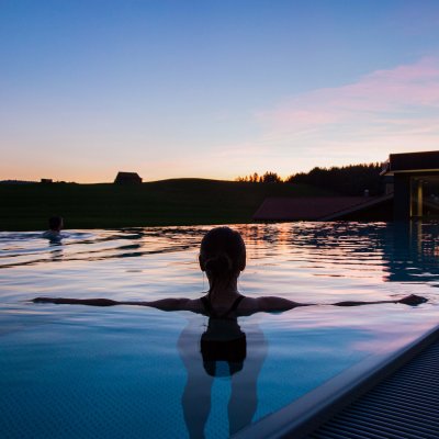 Ein Gast schwimmt in der Abendsonne im Außenpool des Last-Minute-Wellnesshotels im Allgäu.