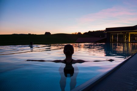 Ein Gast schwimmt in der Abendsonne im Außenpool des Last-Minute-Wellnesshotels im Allgäu.