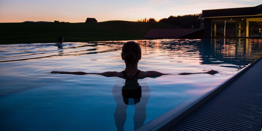 Ein Gast schwimmt in der Abendsonne im Außenpool des Last-Minute-Wellnesshotels im Allgäu.