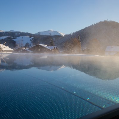 Im Winter steigt Dampf vom beheizten Sportpool des Luxushotels im Allgäu auf, in dem sich die Berge spiegeln.