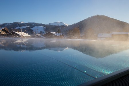 Im Winter steigt Dampf vom beheizten Sportpool des Luxushotels im Allgäu auf, in dem sich die Berge spiegeln.