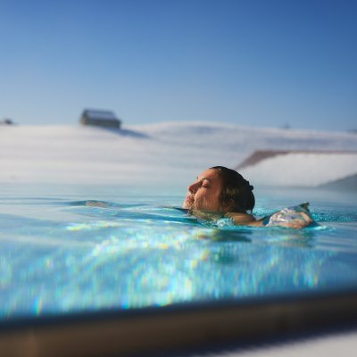 Eine Frau lässt sich im beheizten Außenpool des Wellnesshotels Haubers treiben, das von Schnee umgeben ist.