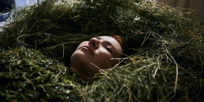 Eine Frau entspannt in Haubers Heubad, bedeckt von feuchtem, warmem Therapieheu.