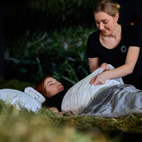 Im Fastenhotel Allgäu legt eine Mitarbeiterin einer Gästin einen Leberwickel mit Therapieheu an.