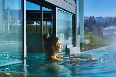Eine Frau schwimmt durch die Poolschleuse in den Außenbereich des Sportpools von Haubers Wellnesshotel.