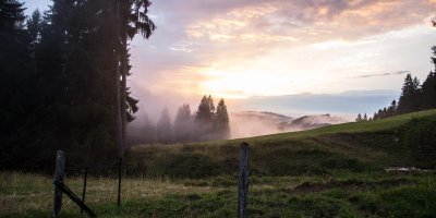 Gewitterwetter färbt den Himmel über den Allgäuer Bergen lila, bevor die Wolken die untergehende Sonne verdecken.