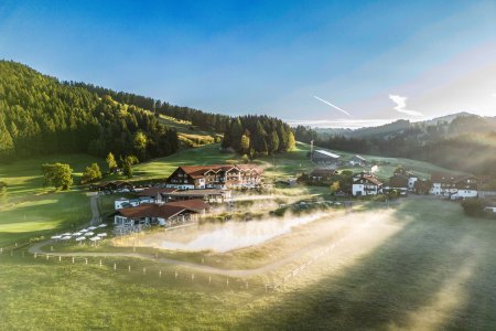 Die Morgensonne fällt auf den Natursee und den Sportpool des Wellnesshotels im Allgäu.