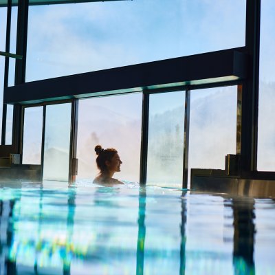 Durch einen Indoor-Einstieg schwimmt eine Gästin in den Außenbereich des Hotel-Pools im Allgäu.