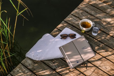 Auf dem Steg des Haubers Natursees liegen Handtuch, Sonnenbrille, Tee und ein Buch im Schatten des Schilfs.