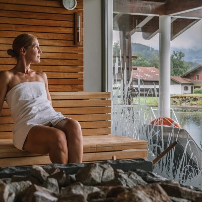 In der Sauna des Haubers Hotels blickt eine Frau im Handtuch über die Berge des Allgäus.