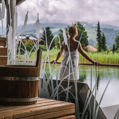 Vor der Hotel-Sauna steht eine Gästin von Haubers Wellnesshotel am Natursee und genießt die Natur.