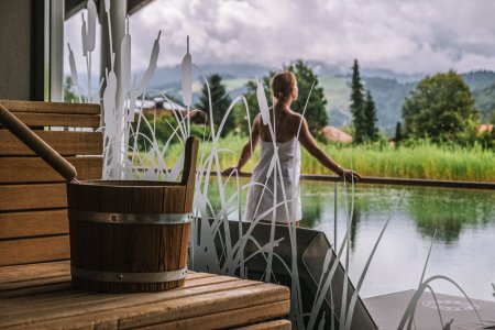 Vor der Hotel-Sauna steht eine Gästin von Haubers Wellnesshotel am Natursee und genießt die Natur.