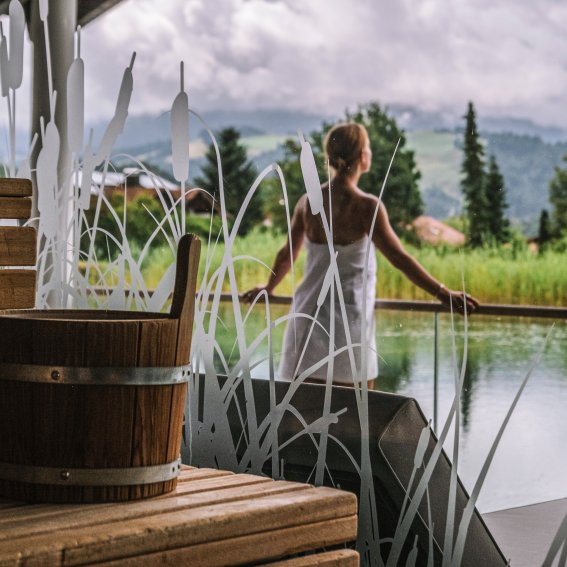 Vor der Hotel-Sauna steht eine Gästin von Haubers Wellnesshotel am Natursee und genießt die Natur.