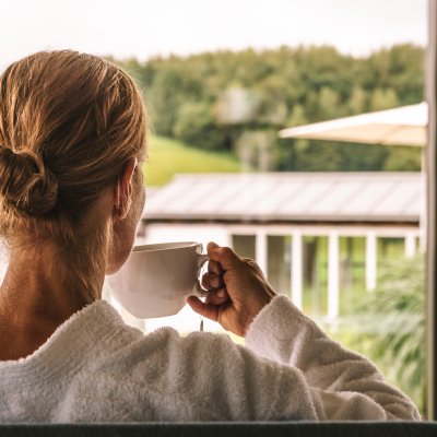 Eine Gästin trinkt Tee und blickt über aus dem Wellnesshotel über das Panorama des Allgäus.