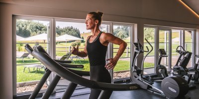 Im hellen Fitnessraum des Sporthotels im Allgäu trainiert eine Frau auf dem Laufband.