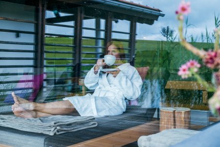 Im Bademantel liegt eine Haubers Gästin im Ruheraum und trinkt eine Tasse Tee.