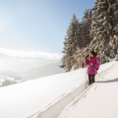 Beim Winterwandern blickt eine Frau über das 4-Sterne-Hotel nach Oberstaufen im Allgäu.