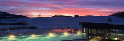 Im Sportpool des Fastenhotels schwimmt ein Gast vor dem Abendrot, das sich hinter den Allgäuer Bergen abzeichnet.