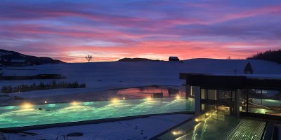 Im Sportpool des Fastenhotels schwimmt ein Gast vor dem Abendrot, das sich hinter den Allgäuer Bergen abzeichnet.