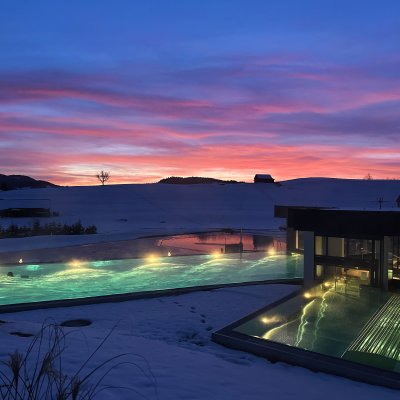 Im Sportpool des Fastenhotels schwimmt ein Gast vor dem Abendrot, das sich hinter den Allgäuer Bergen abzeichnet.