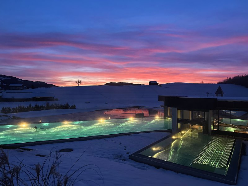 Im Sportpool des Fastenhotels schwimmt ein Gast vor dem Abendrot, das sich hinter den Allgäuer Bergen abzeichnet.