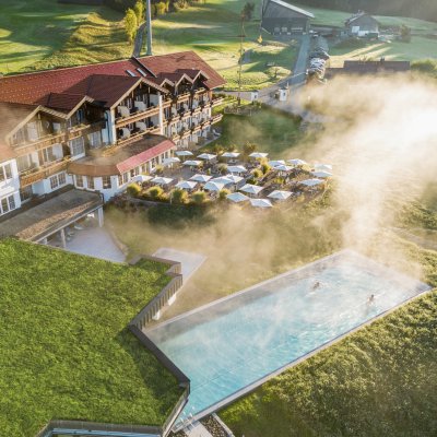 Zwei Gäste schwimmen im Sportpool von Haubers Wellnesshotel, während Morgennebel über die Sonnenterrasse zieht.