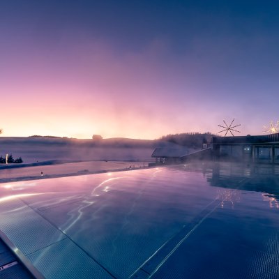 Der Sportpool des Haubers Wellnesshotels liegt im romantischen Abendrot vor Allgäuer Bergkuppen.