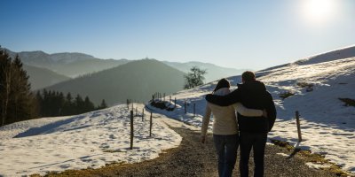 Ein Paar spaziert Arm in Arm durch den Schnee auf das Romantikhotel im Allgäu zu.