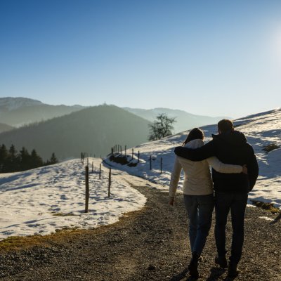 Ein Paar spaziert Arm in Arm durch den Schnee auf das Romantikhotel im Allgäu zu.