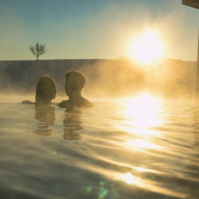 Die Wintersonne scheint auf ein Paar, das im beheizten Außenpool von Haubers Wellnesshotel die Wärme genießt.