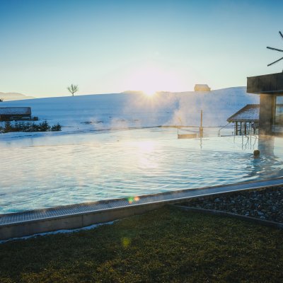 Ein Gast schwimmt im Sportpool des Wellnesshotels im Allgäu, während die Abendsonne hinter den Bergen untergeht.