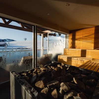 Aus der großen Sauna in Haubers Wellnesshotel blicken Gäste über den Natursee und die verschneiten Berge des Allgäus.