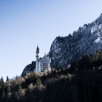 Schloss Neuschwanstein im Winterlicht am Berghang in Bayern. Das malerische Schloss Neuschwanstein erhebt sich im Winter über den verschneiten Bergen in Bayern, umgeben von kühlem, blauem Himmel.