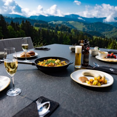 Der sonnenbeschienene Frühstückstisch von Haubers Gästen ist mit Bratkartoffeln, Weißwurst und Bier gedeckt.