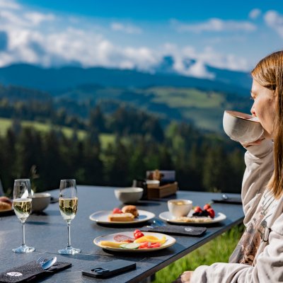 Eine Frau sitzt bei Sonnenschein am Tisch vor Haubers Schwalbennest und trinkt Tee.