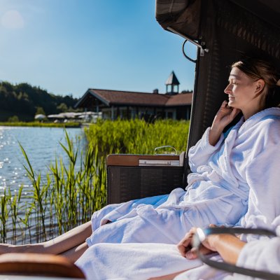 Zwei Gäste sitzen in Bademänteln im Strandkorb an Haubers Natursee und genießen die Sonne auf der Haut.