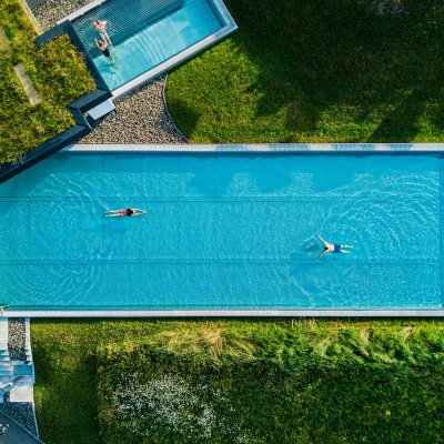 Schwimmer genießen entspanntes Wasservergnügen Zwei Personen schwimmen entspannt im blauen Wasser eines langen Pools an einem sonnigen Tag umgeben von Grün.