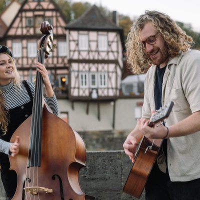 Fruit Sharks spielen vor Fachwerkhäusern im Allgäu. Marlene am Kontrabass und Oli an der Gitarre sind die Band Fruit Sharks, fotografiert von Simon Kübler.