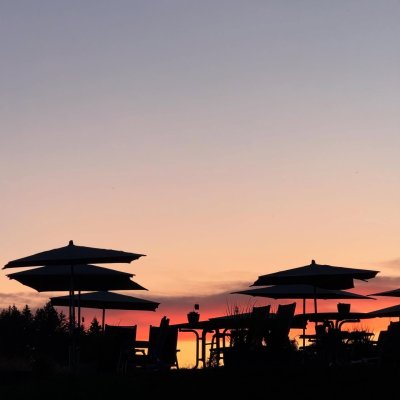 Die Silhouetten von Tischen und Sonnenschirmen bei Sonnenuntergang laden zum Entspannen in der Natur ein.
