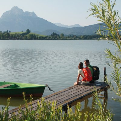 Zwei Wanderer sitzen am Forggensee bei Füssen, fotografiert von Gerhard Eisenschink für Füssen Tourismus.
