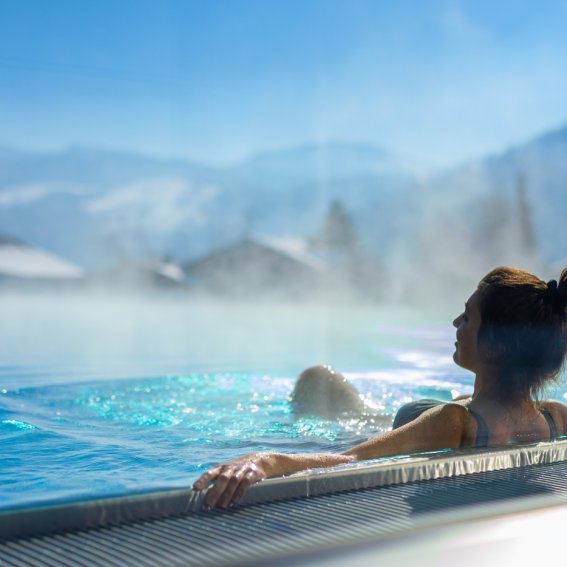 Eine Frau entspannt im warmen Relaxpool von Haubers Naturresort. Entspannung im beheizten Relaxpool während dem Wellnessurlaub im Haubers Naturresort, mit Blick auf die Berg-Kulisse.
