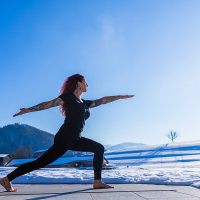 Eine Yoga-Teilnehmerin in Kriegerpose im Winter. Eine Yoga-Teilnehmerin im Winter in Yoga-Pose.