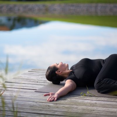 Die Teilnehmerin eines Yoga-Kurses dehnt sich am Randes des Natursees von Haubers Naturresort.