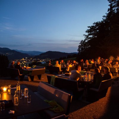 Haubers Gäste genießen die Köstlichkeiten der Gourmetküche bei Kulinarik am Schwalbennest mit Blick auf das nächtliche Panorama.