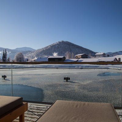 Der eisbedeckte Natursee von Haubers Wellnesshotel glitzert in der Allgäuer Wintersonne.