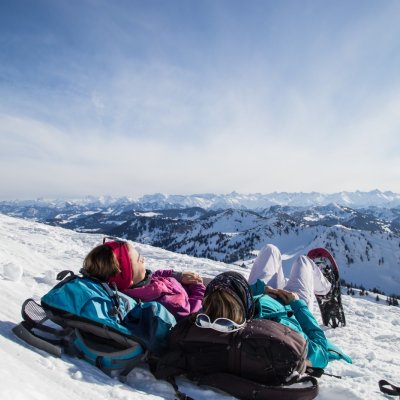 Zwei Gästinnen genießen den Ausblick ins Allgäu bei einer Pause auf ihrer Schneeschuhwanderung.