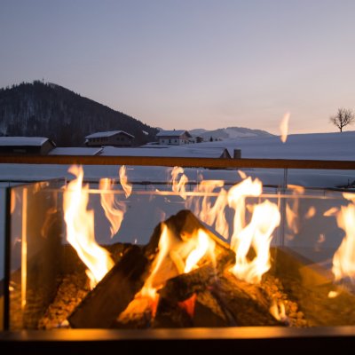 Auf der Terrasse des Haubers Wellnessbereichs brennt ein Feuer vor dem verschneiten Panorama der Allgäuer Berge.