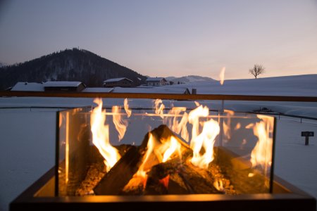 Auf der Terrasse des Haubers Wellnessbereichs brennt ein Feuer vor dem verschneiten Panorama der Allgäuer Berge.