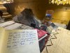 Ein Buch liegt auf einem Tisch mit Steinen und Holz Ein offenes Buch liegt auf einem Tisch. Daneben liegen Steine und Holz. Es gibt auch einige Broschüren und eine Lampe.
