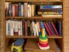 Bücherregal mit Spielzeug auf dem Tisch Das Regal steht in einem Raum. Es ist voll mit Büchern. Ein Stapel Spielzeug steht auf einem Tisch.